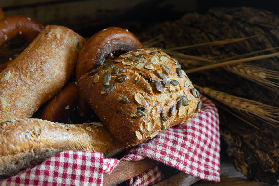 frische brötchen und laugengebäck im korb auf rot-weißem tuch mit getreideähren frische brötchen und laugengebäck im korb auf rot-weißem tuch mit getreideähren
