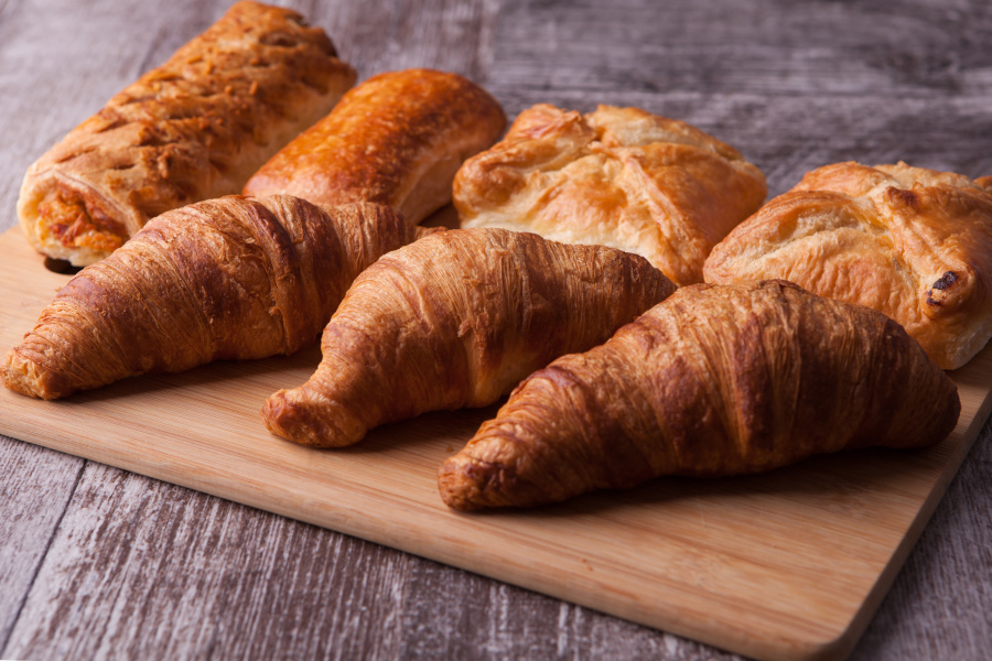 frische croissants und blätterteiggebäck auf einem holzbrett angerichtet